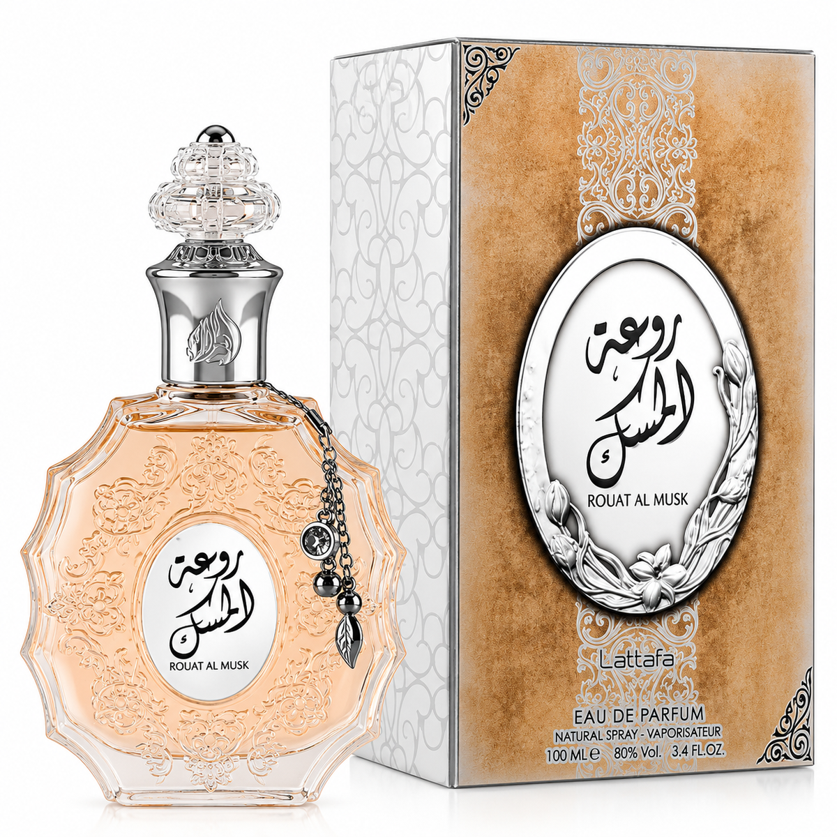 A bottle of Rouat Al Musk Eau de Parfum next to its retail box. The perfume bottle is clear glass filled with a pale peach-pink liquid, featuring an ornate silver-tone cap and a hanging silver charm.